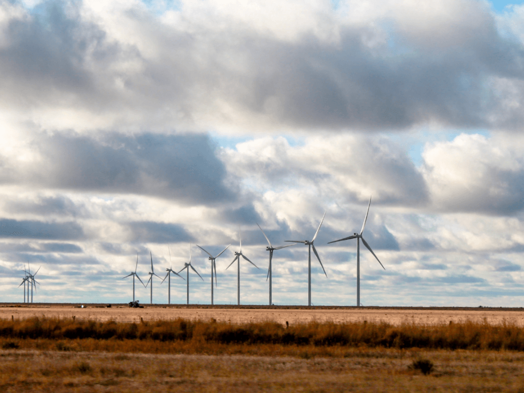 Wide view of wind turbines across open plains under a cloudy sky, symbolizing renewable energy innovation and the full lifecycle of wind farm operations, from generation to responsible decommissioning.